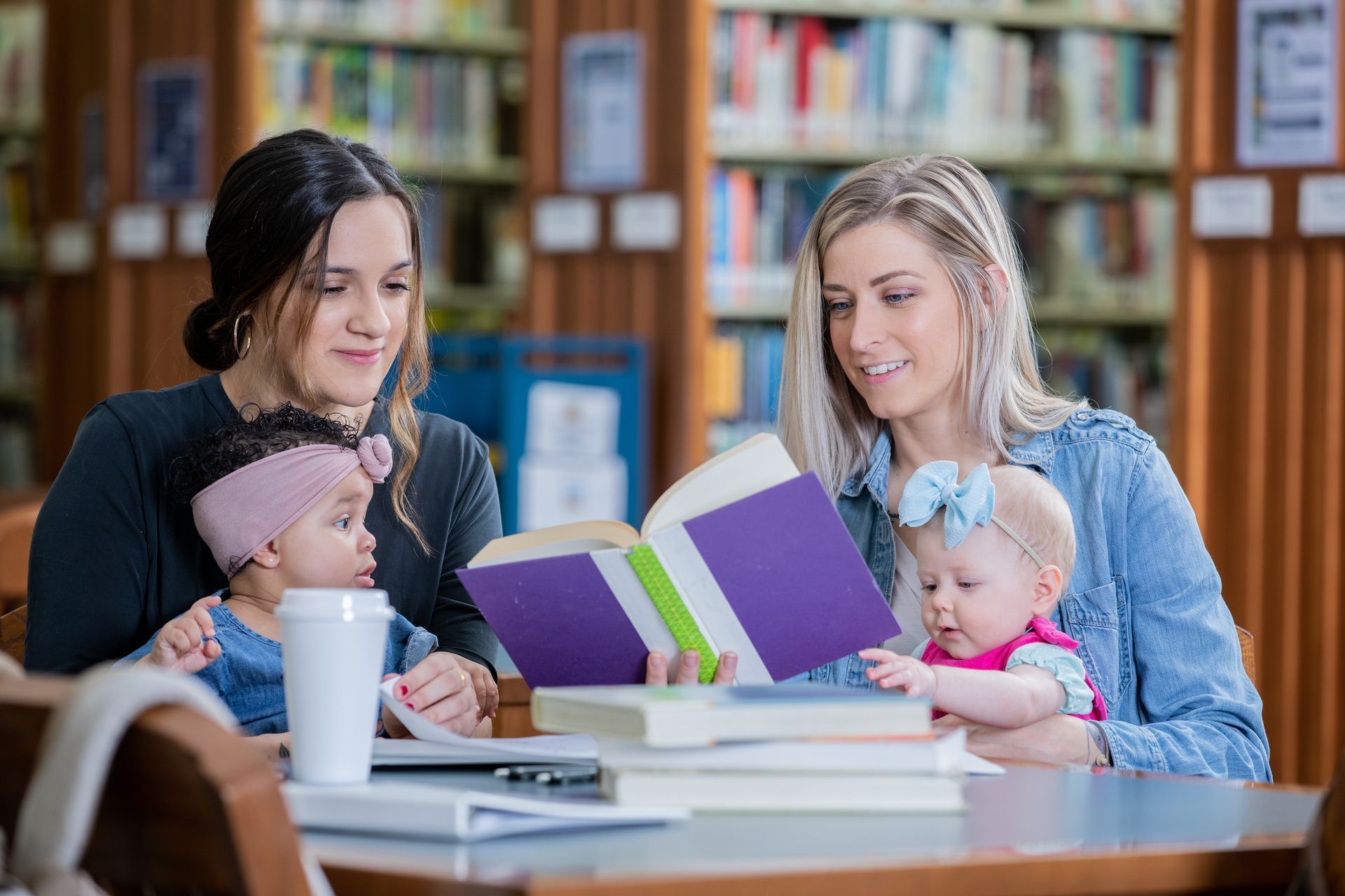 Two women and a baby are reading books in a library.