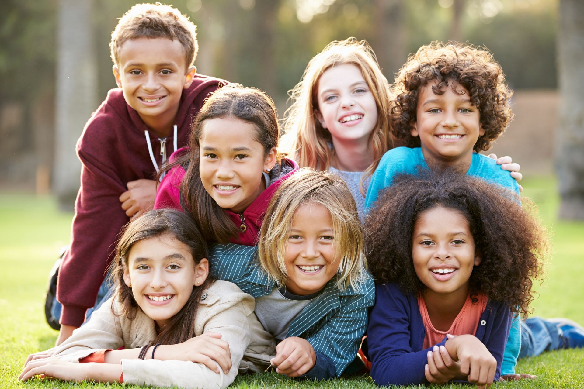 A group of children are laying on top of each other on the grass.