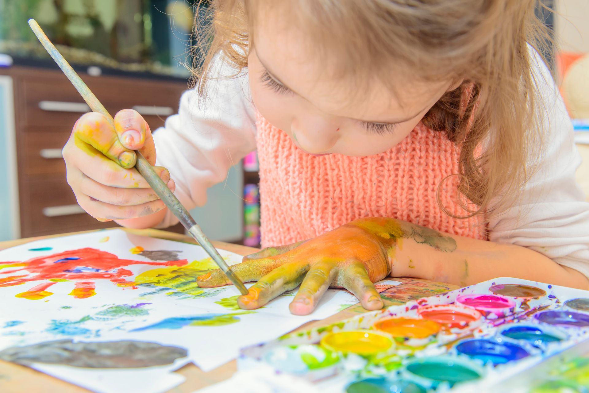 Child painting with colorful watercolor paints on paper at a table