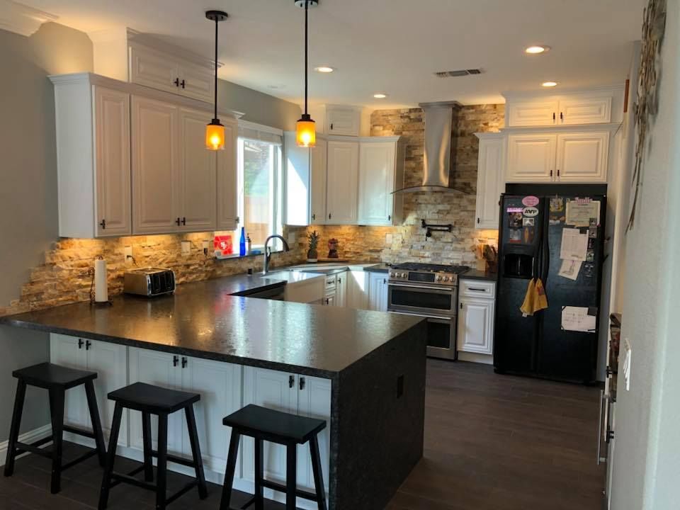 A kitchen with white cabinets , black appliances , a large island and stools.