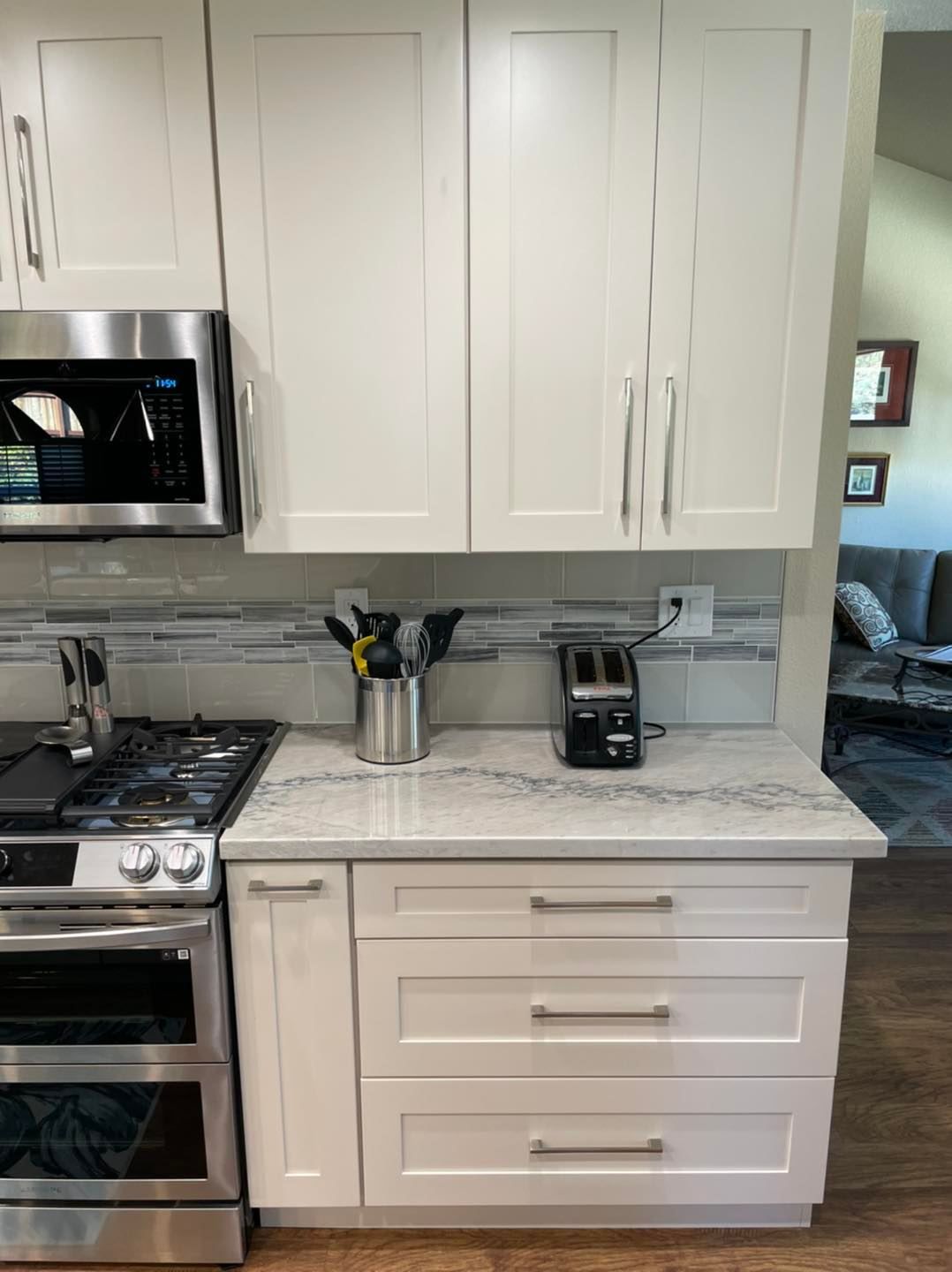 A kitchen with white cabinets , a stove , a microwave , and a toaster oven.