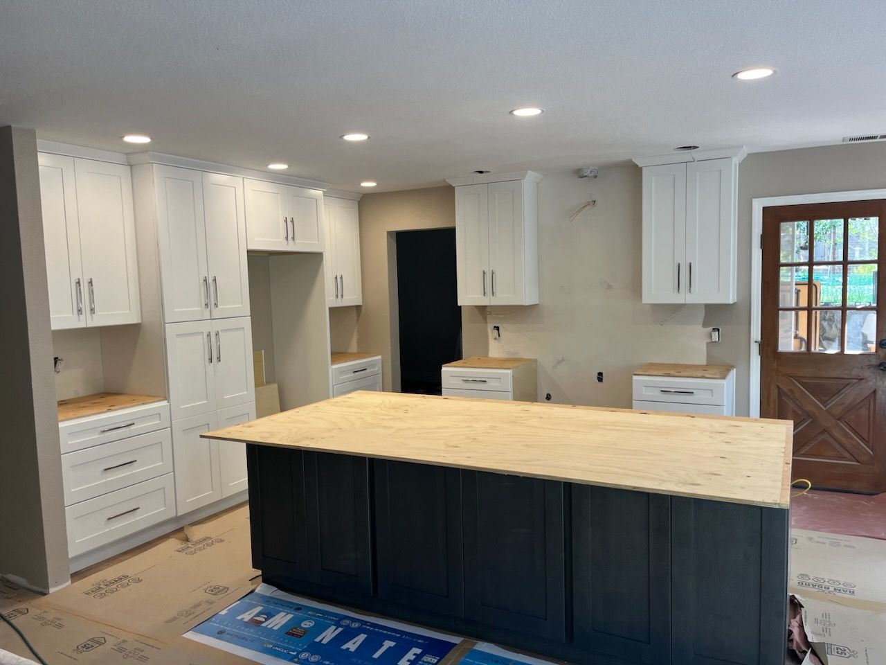A newly renovated kitchen featuring white cabinets, a dark gray island, and a light wood countertop.