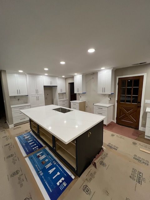 A newly renovated kitchen with white cabinets and a large dark-colored island with a white countertop.