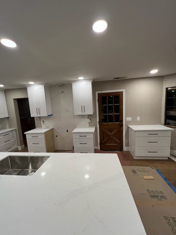 Kitchen remodel in progress: white cabinets installed, white countertop island, unfinished walls, brown door.