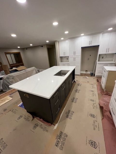 A kitchen renovation in progress with a dark brown island, white countertops, and unfinished cabinets against white walls.