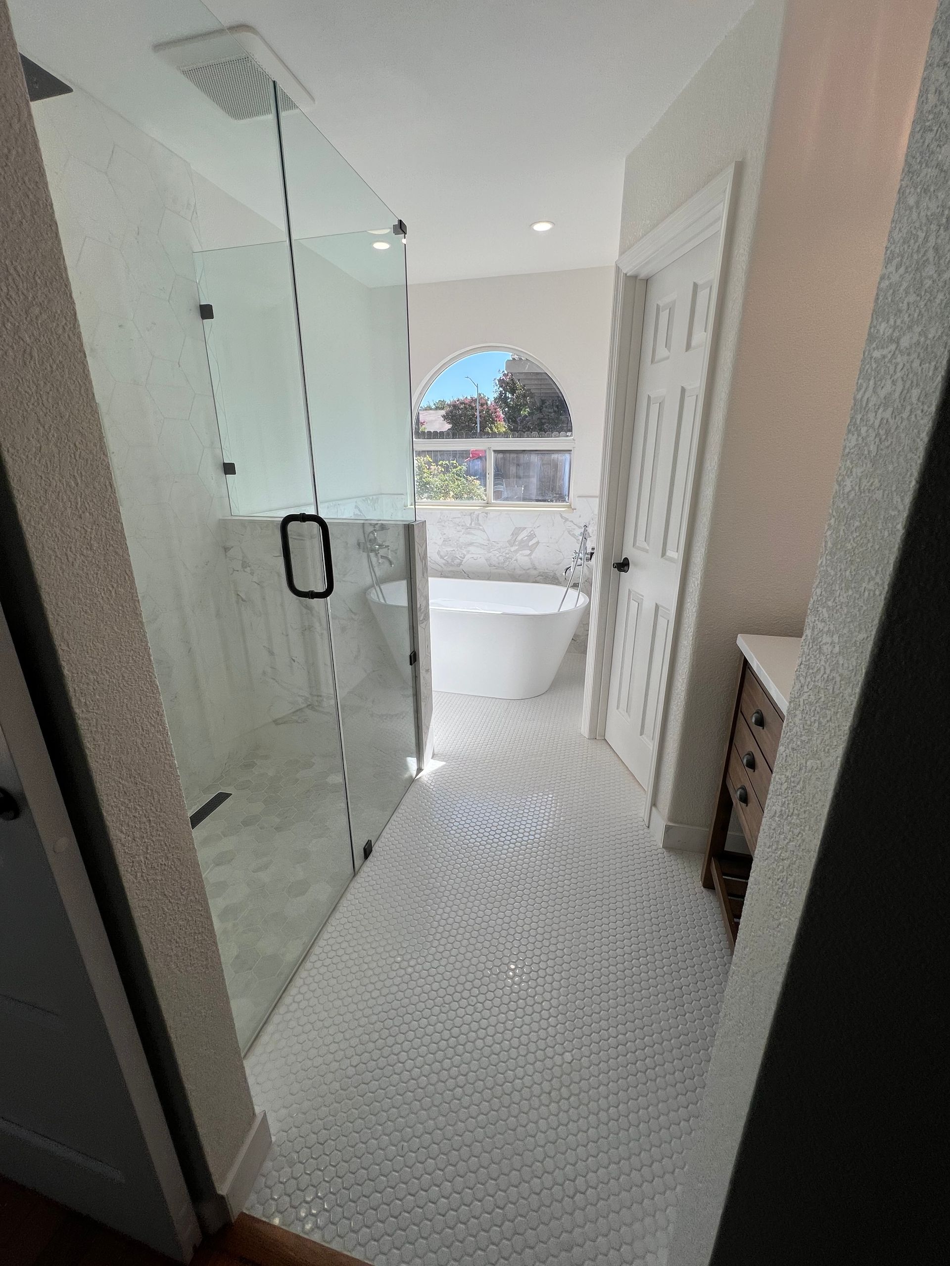 Bright white bathroom with a glass shower, soaking tub, and white patterned floor.