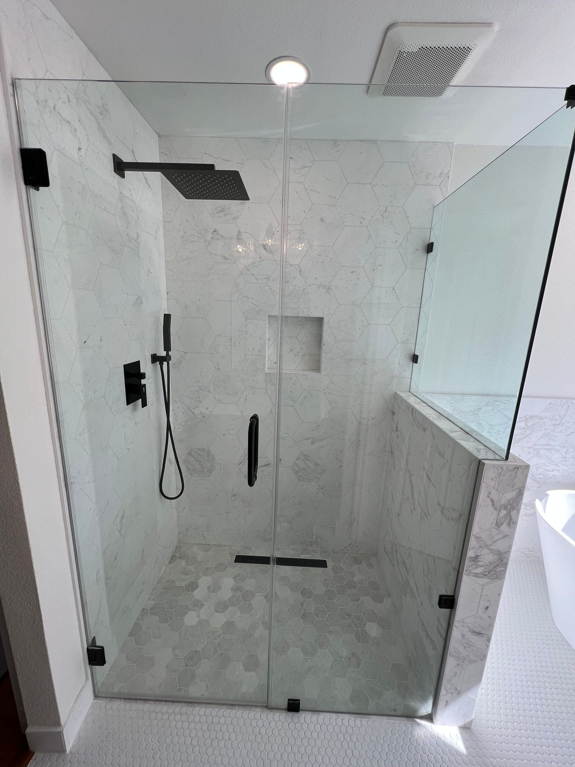 Modern shower with a glass enclosure and black hardware against a marble-tiled backdrop.