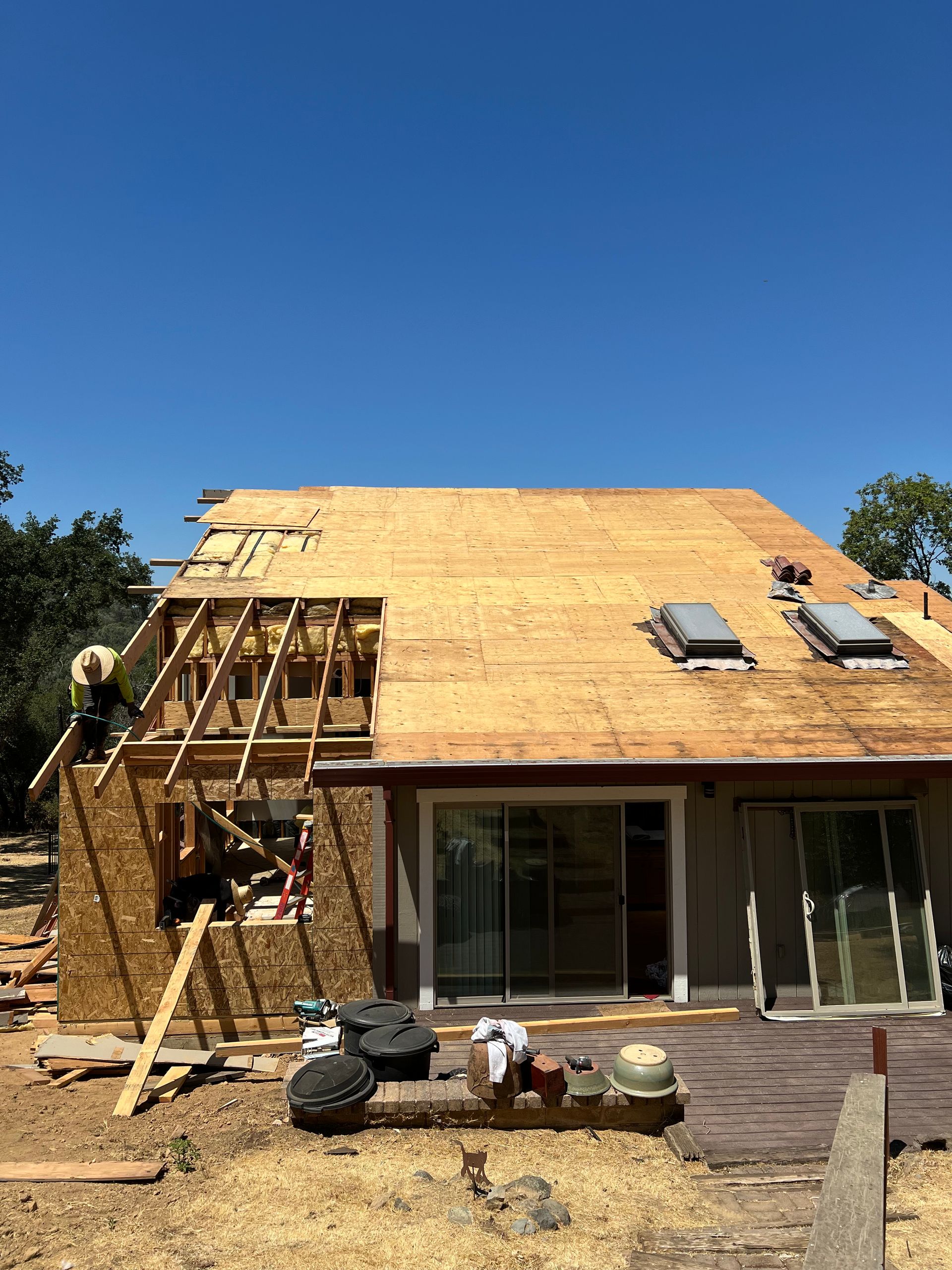 Construction workers on a roof removing old shingles. A partially built wooden structure with exposed beams.