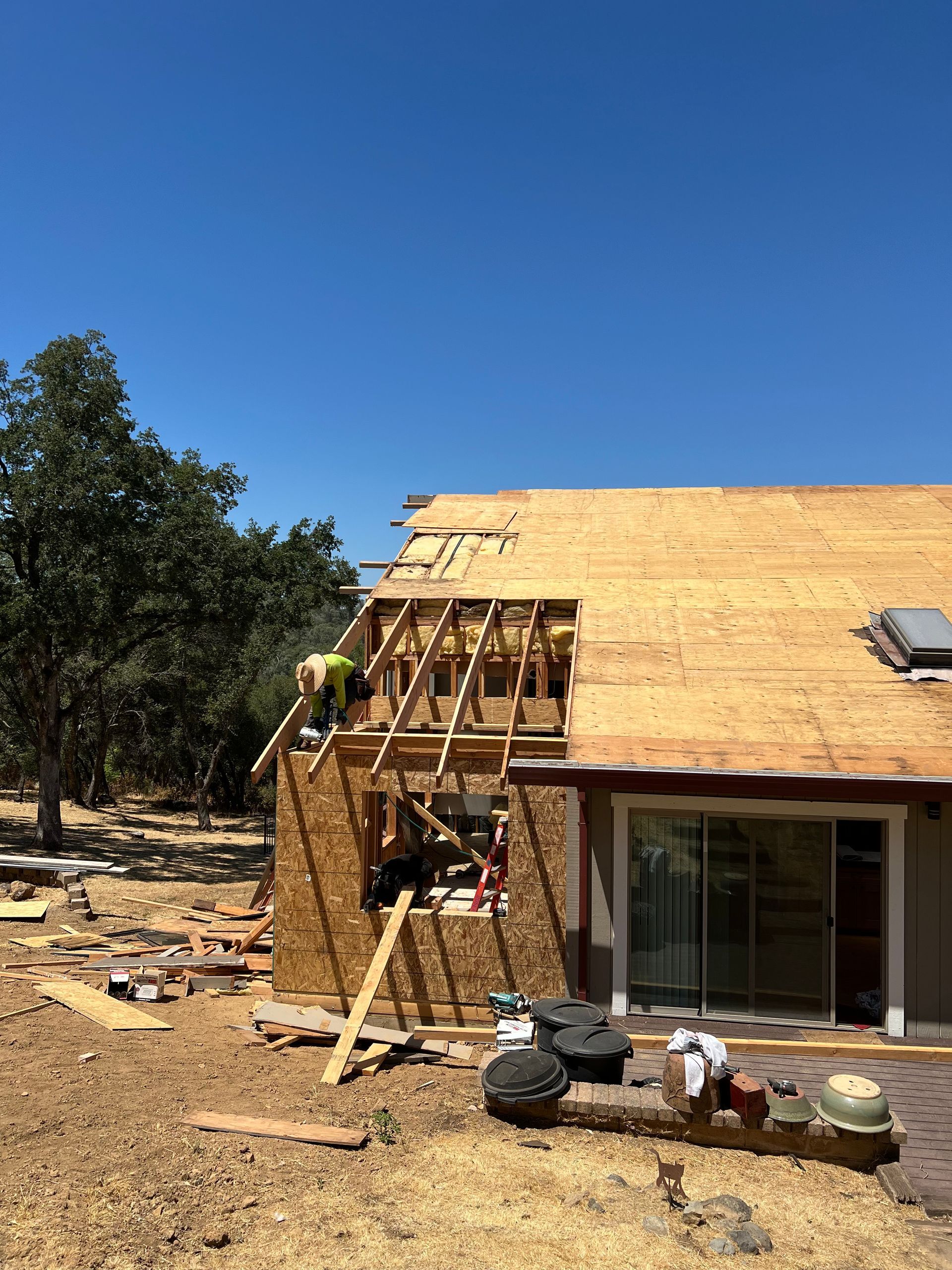 Construction workers building a new roof on a house, removing old materials. Bright blue sky.