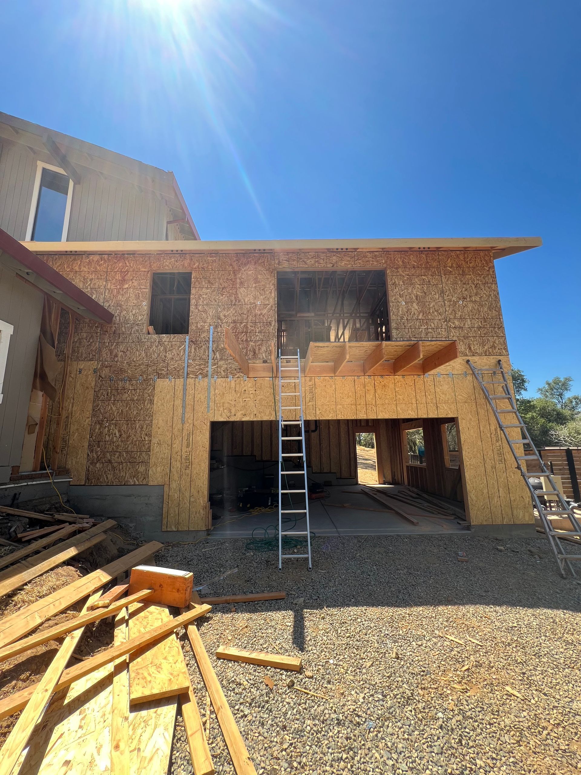 Garage under construction with wood framework and plywood siding against a blue sky. A ladder stands in the garage opening.