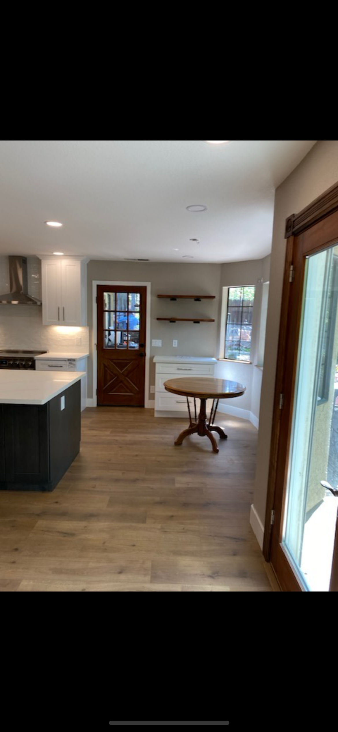 A renovated kitchen with wood floors, a dark island, and a wooden round table. A rustic wooden door.
