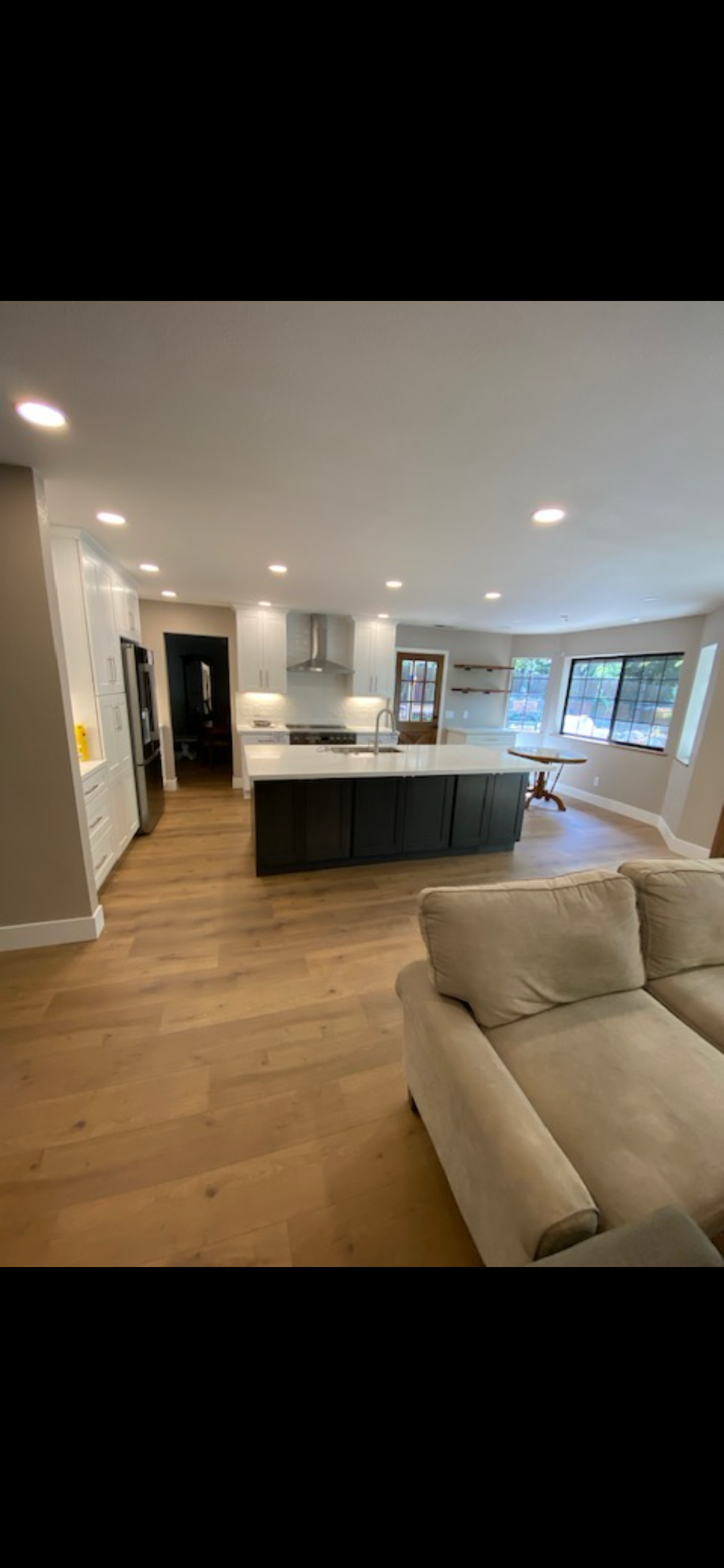 A modern kitchen with dark cabinetry, a large island, and light wood floors. The room is open-plan.