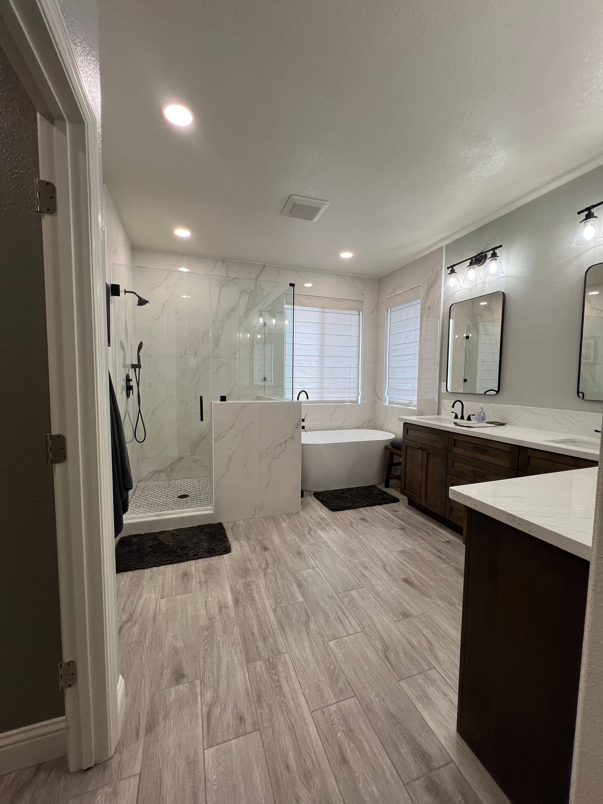 Spacious modern bathroom with a shower, freestanding tub, double vanity, and wood-look tile flooring.