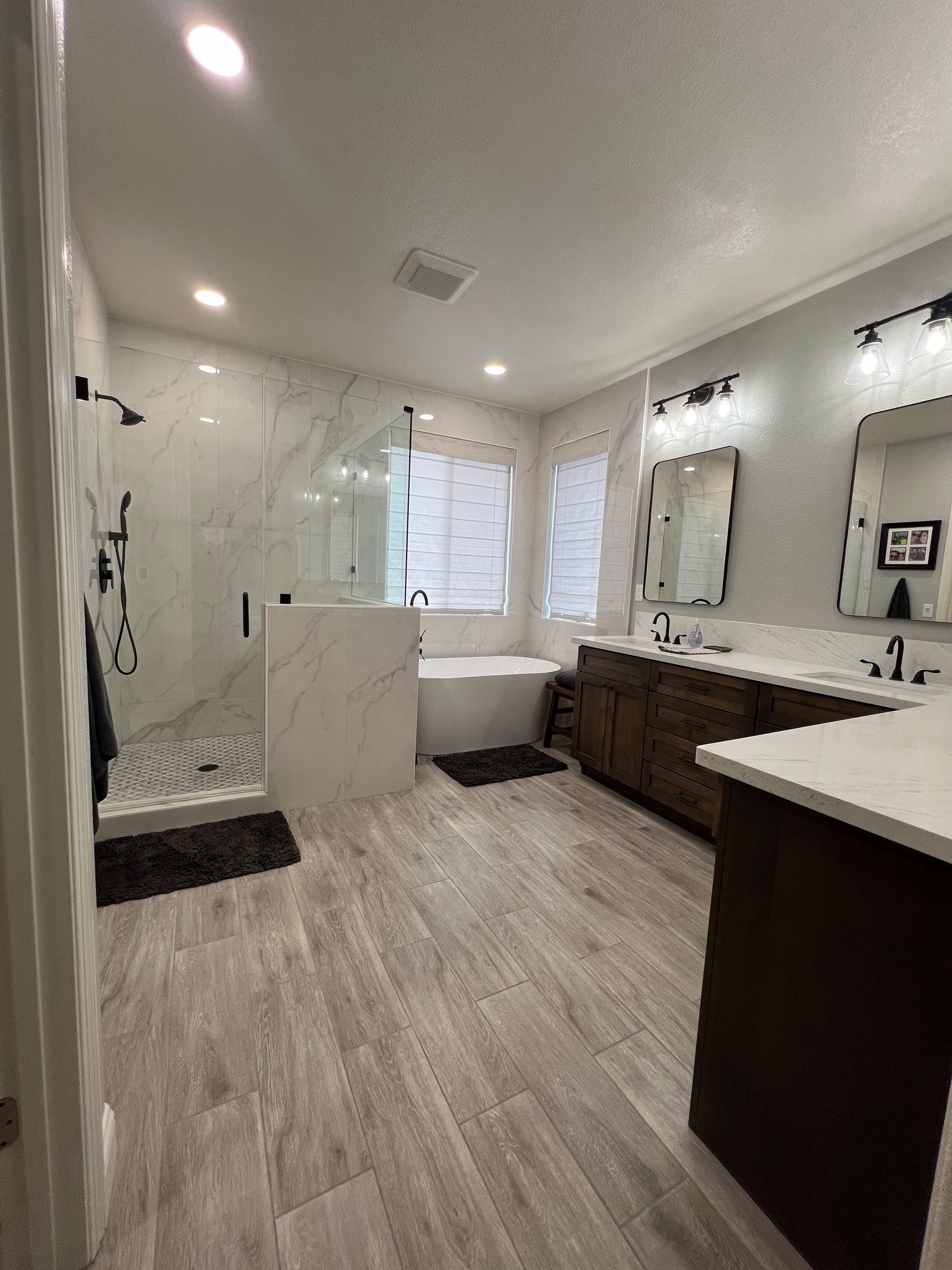 Spacious modern bathroom with marble shower, wood vanity, and soaking tub. Neutral tones and good lighting.