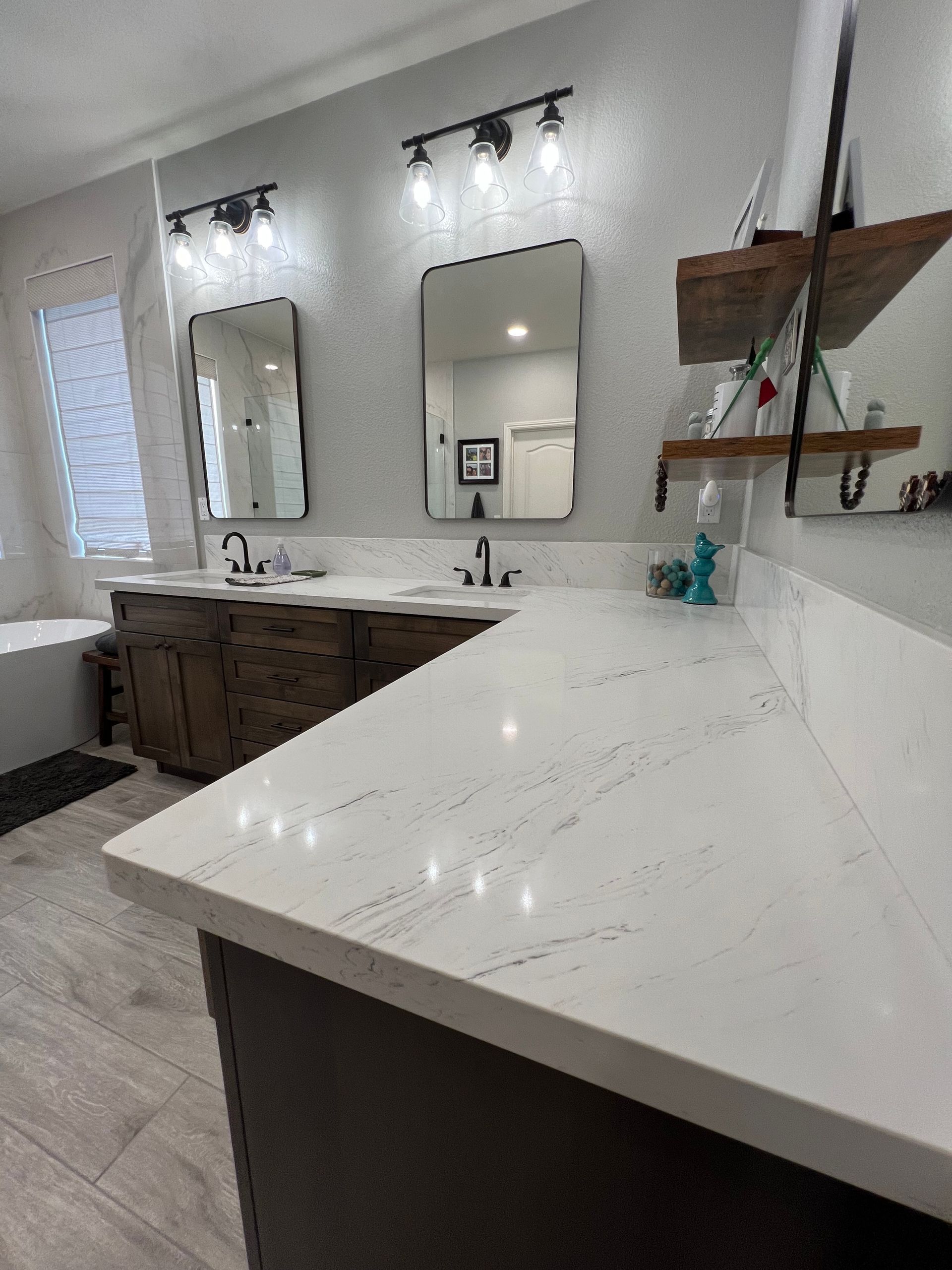 Bathroom with white countertop, dark brown cabinets, two mirrors with black frames, and open wooden shelves.