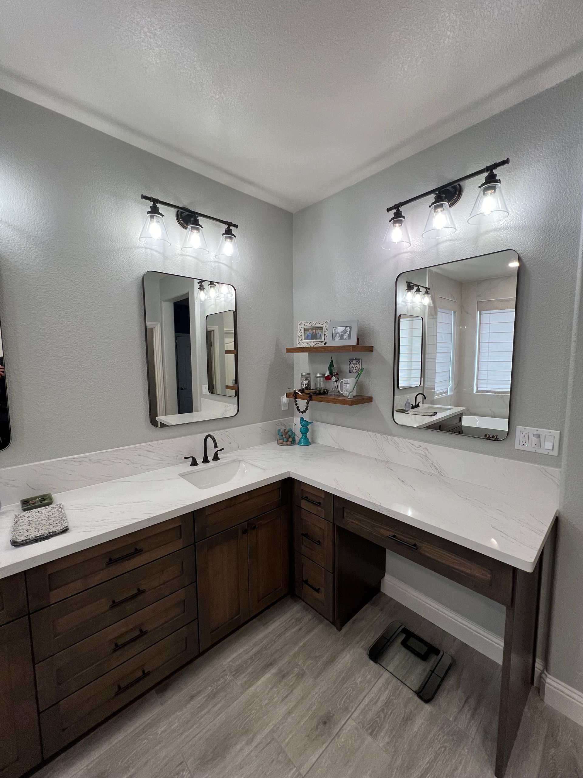 Bathroom with dark wood cabinets, light countertops, two mirrors, and gray walls. Two light fixtures over the mirrors.