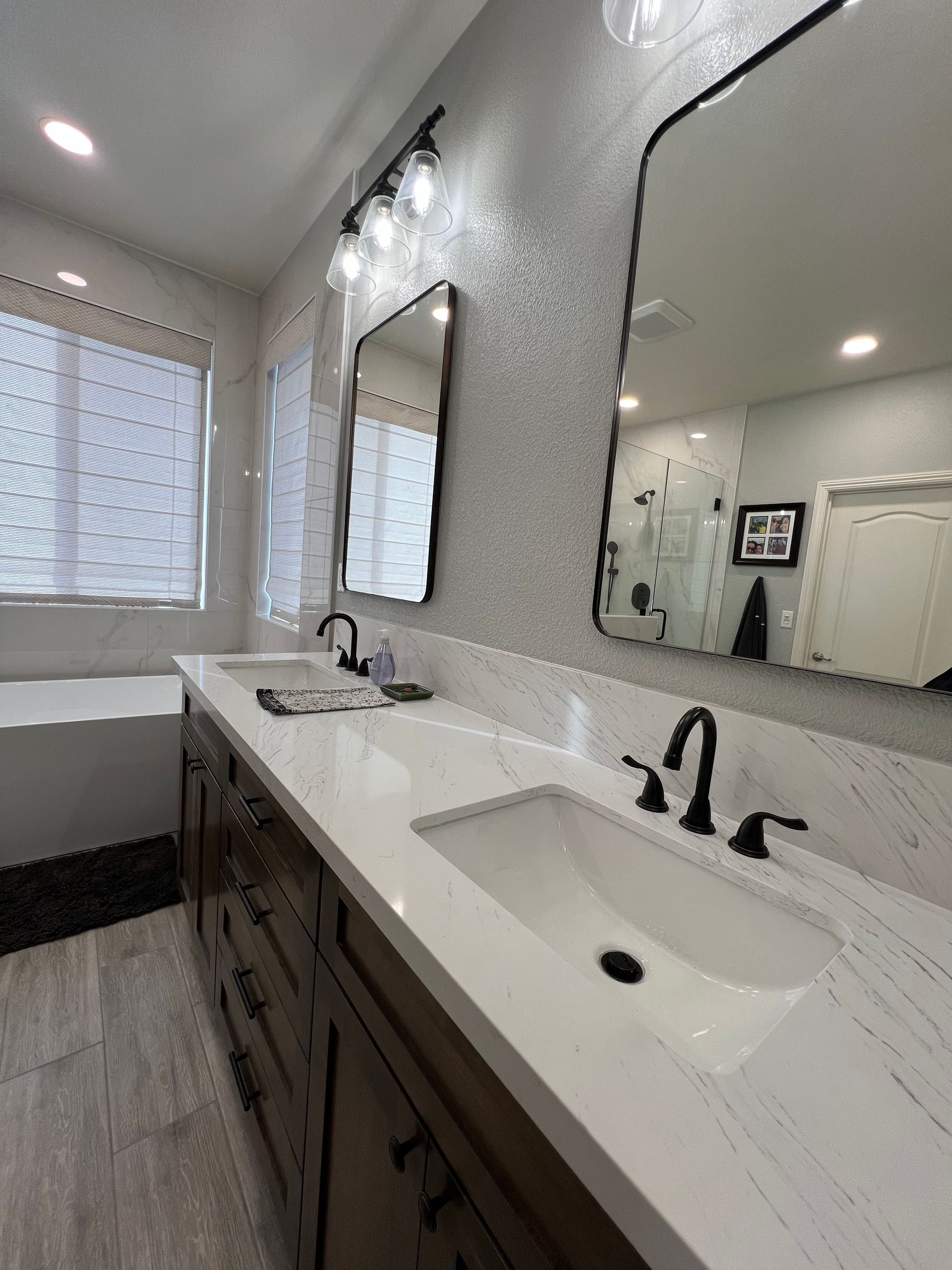 A modern bathroom with a double vanity, two mirrors, and white countertops. Dark wood cabinets contrast with the light walls.