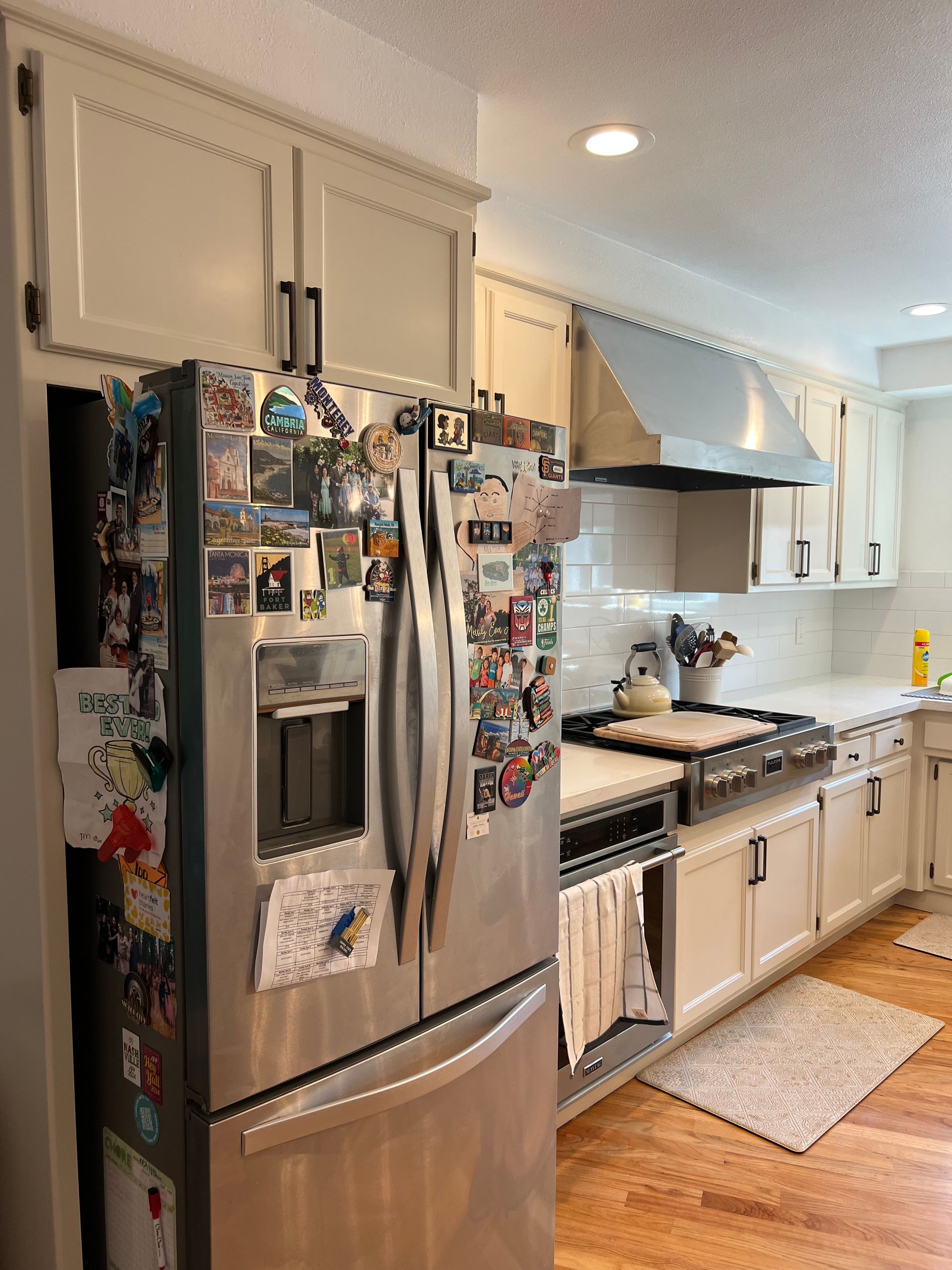 A kitchen with stainless steel appliances and cream-colored cabinets. The refrigerator door is covered in magnets.