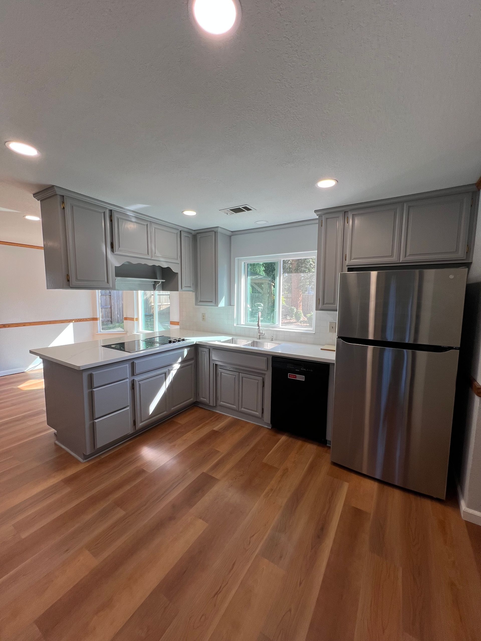 Gray kitchen with white countertops, stainless steel appliances, and wood floors.
