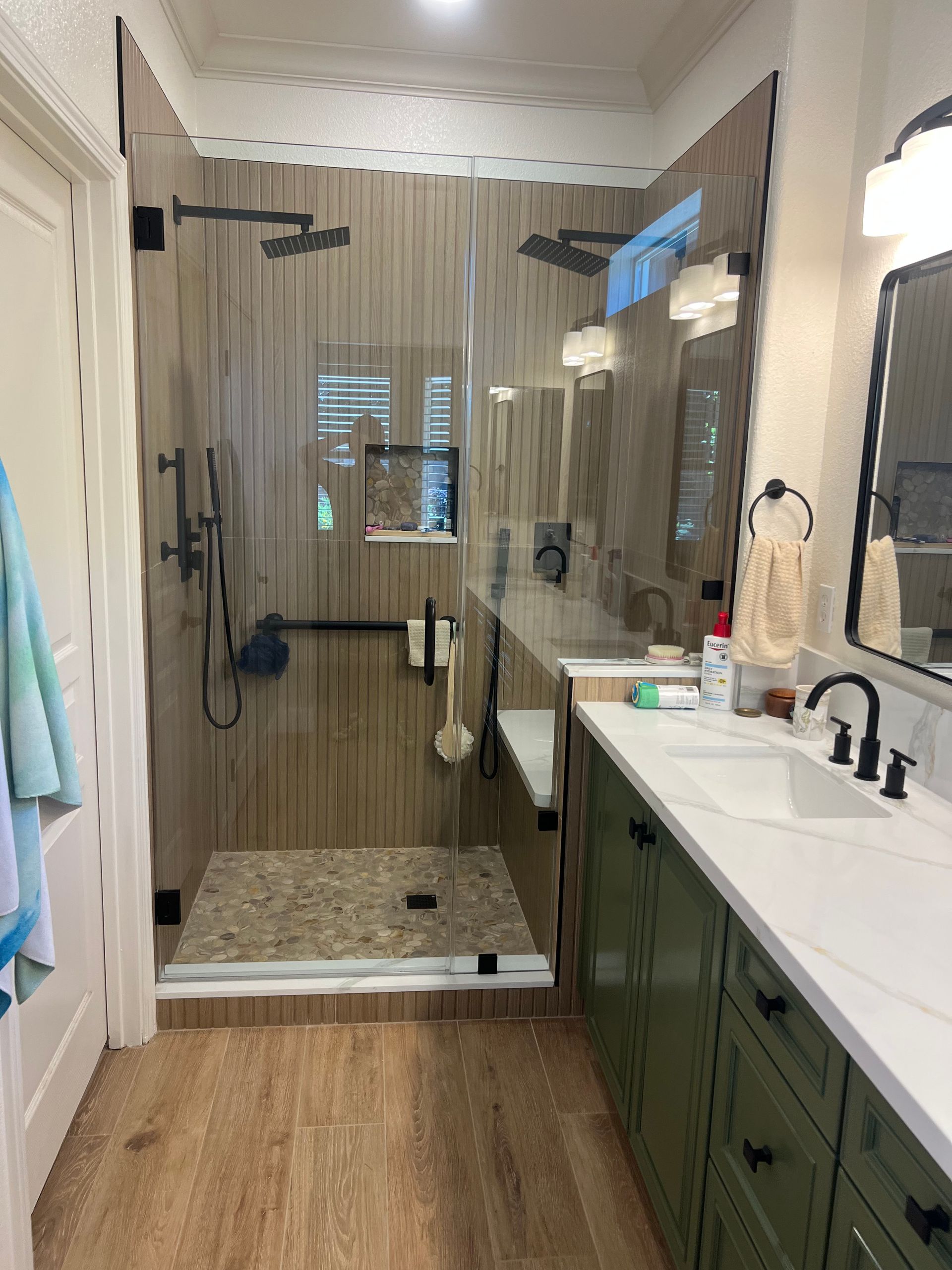 Bathroom with a glass-enclosed shower featuring stone floor and wooden panel walls. A vanity with green cabinets.