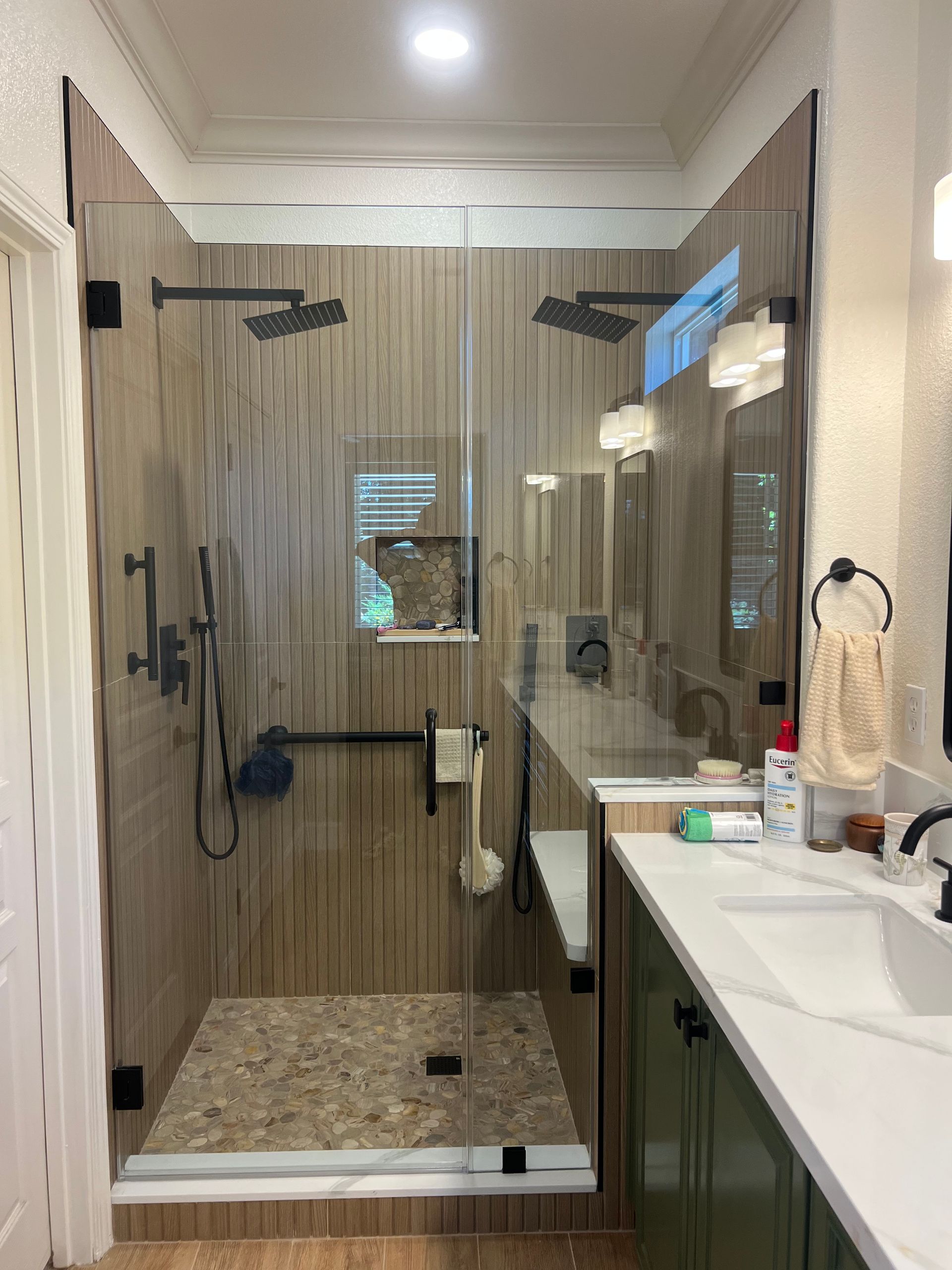 A modern bathroom with a glass shower enclosure. Brown vertical tile lines the shower walls and the floor is stone-like.