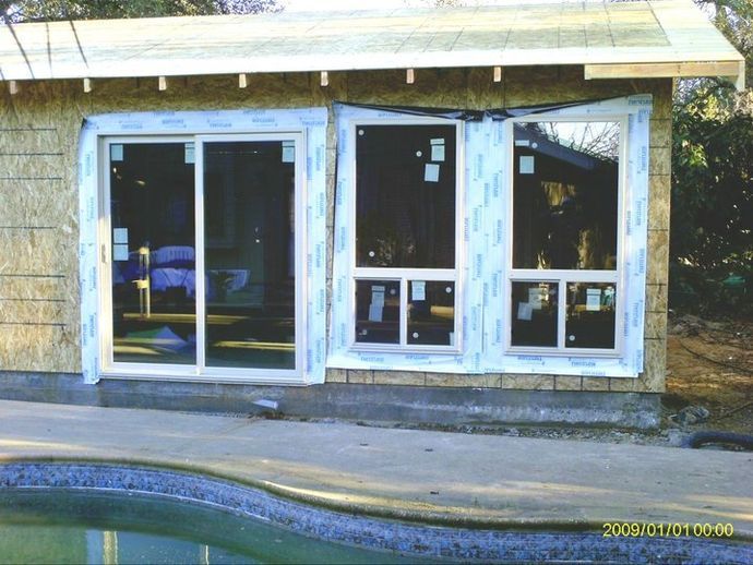 A house with sliding glass doors is being built next to a pool