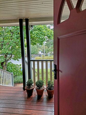Front porch with red door, potted plants, and white railing overlooking green trees