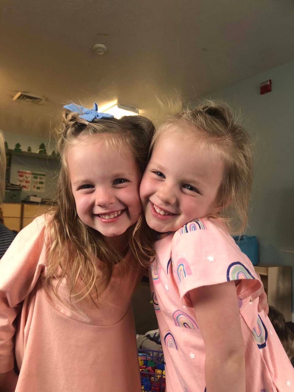 Two smiling children leaning cheek to cheek in a warmly lit room