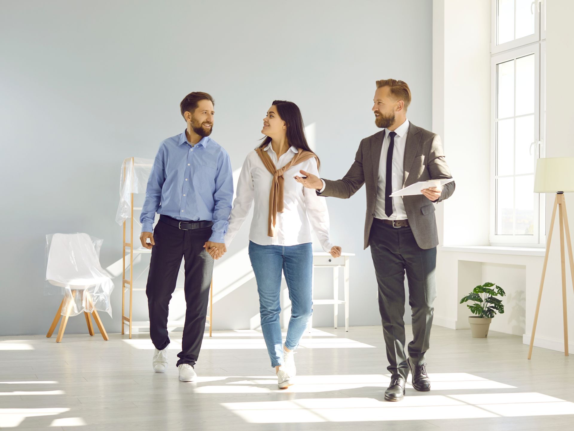 Real estate agent shows couple a potential home's empty, light-filled room.