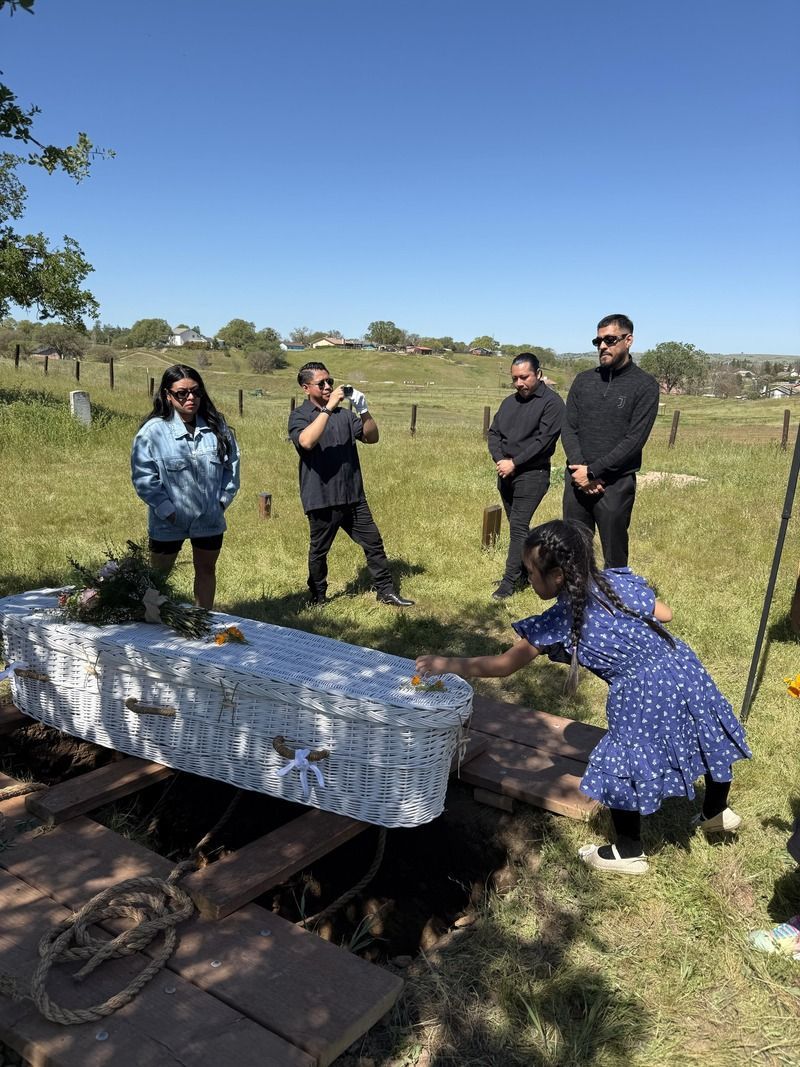 People inspecting a large white object in a grassy field near a fence under a clear blue sky