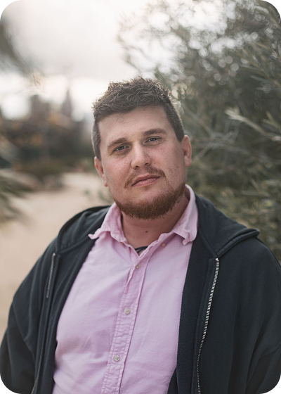 Portrait of a person in a pink shirt and dark jacket standing outdoors with a blurred background