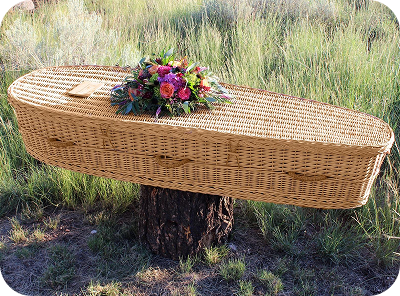 Woven wicker coffin with flowers resting on a tree stump in a grassy field