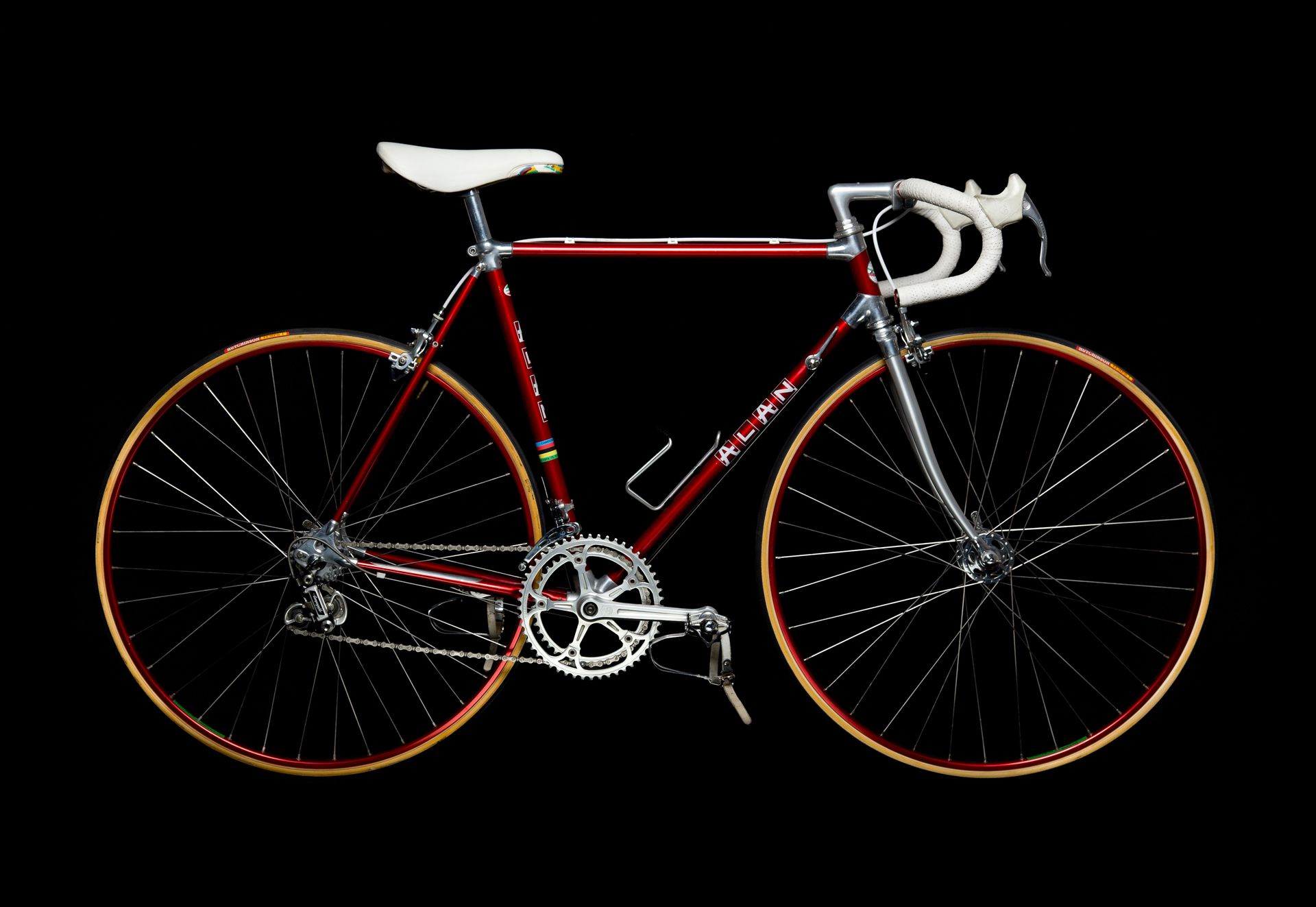 Red vintage road bicycle with white seat and handlebars against a black background.