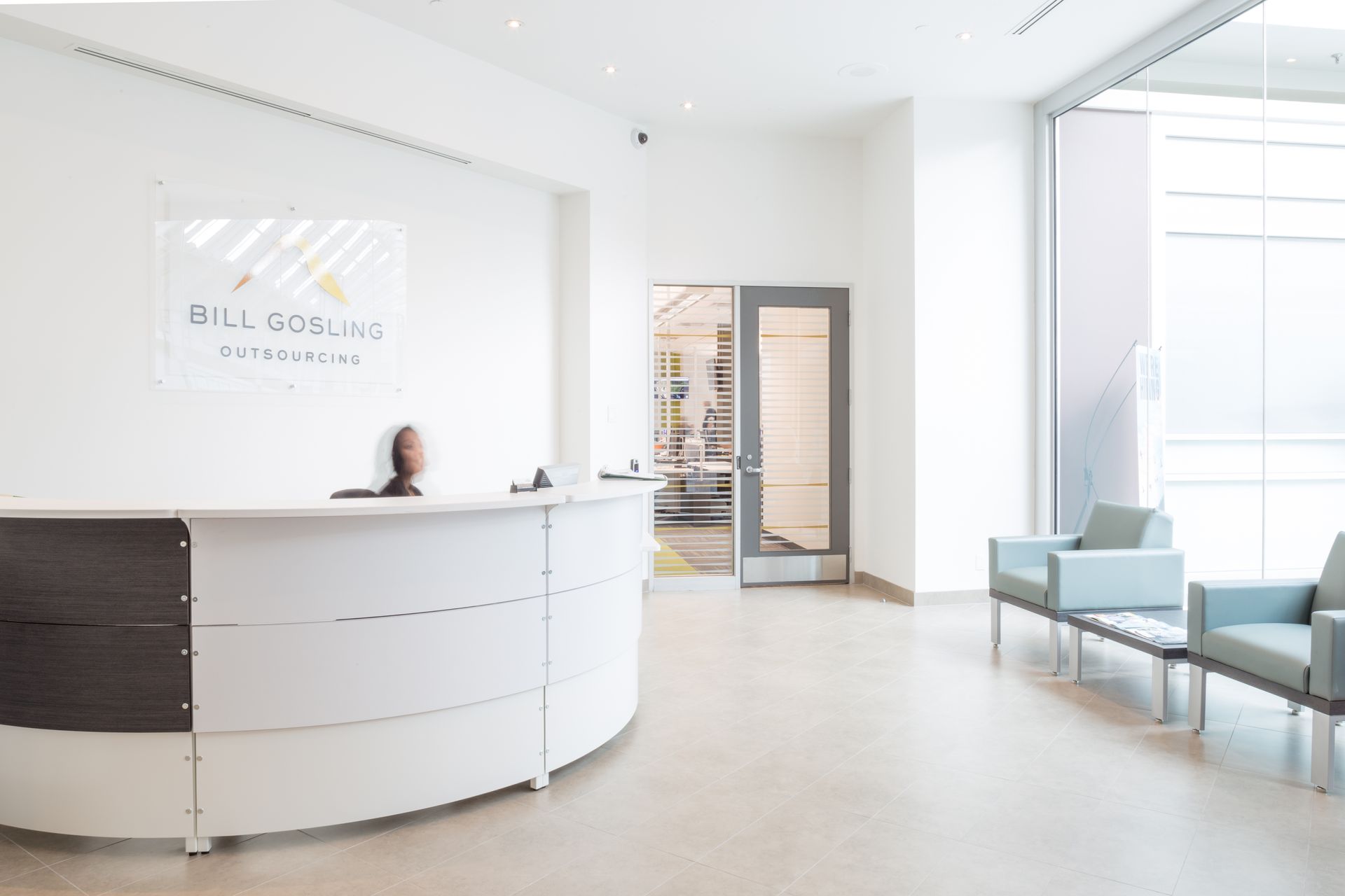 Modern office reception area with curved white desk, chairs, and logo on the wall.