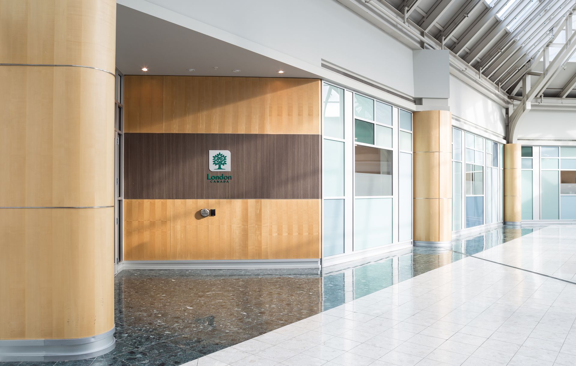 An entrance with wood panels, logo, and glass storefront in a modern, light-filled corridor.