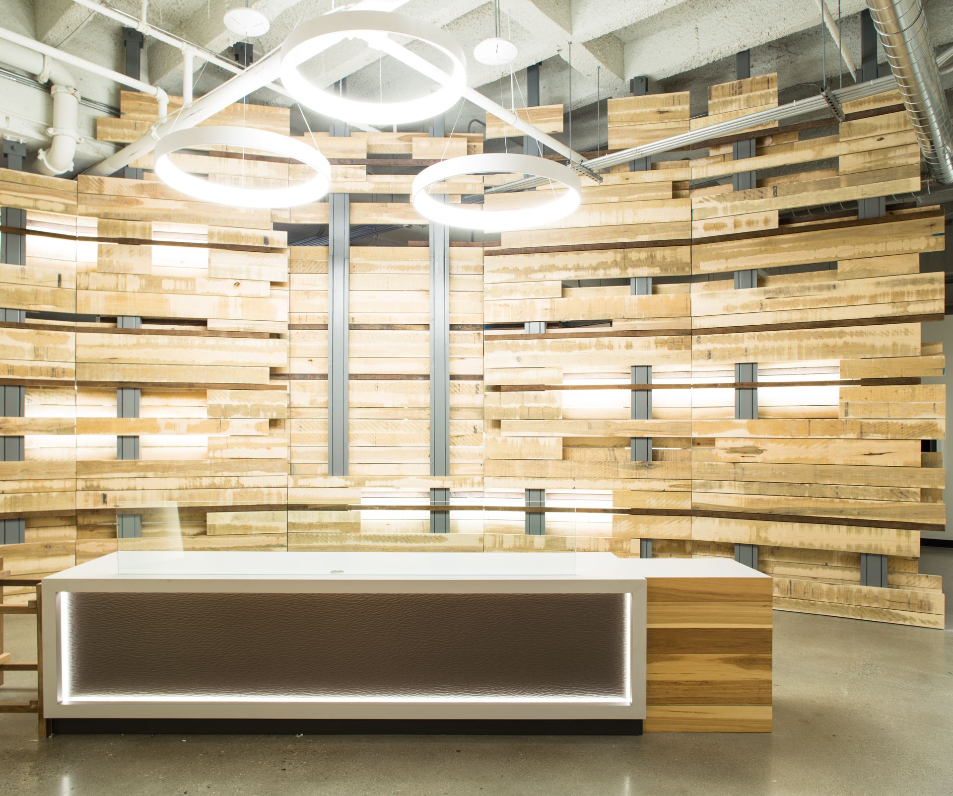 Reception area with wooden wall backdrop, modern desk with led lighting, and ring-shaped ceiling lights.