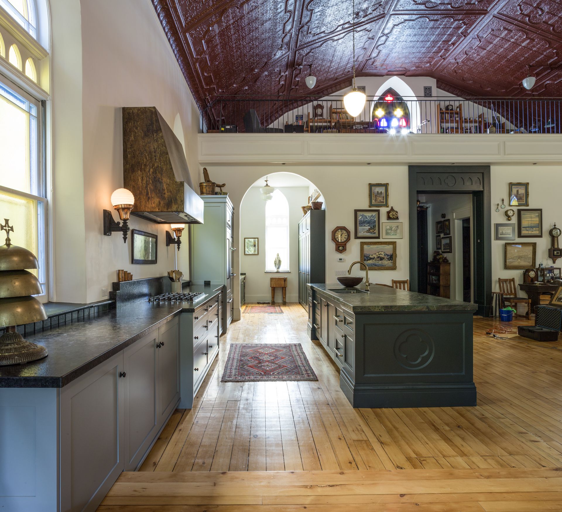 Spacious kitchen with wood floors, island, and long counter, inside a building with a high, red-patterned ceiling.
