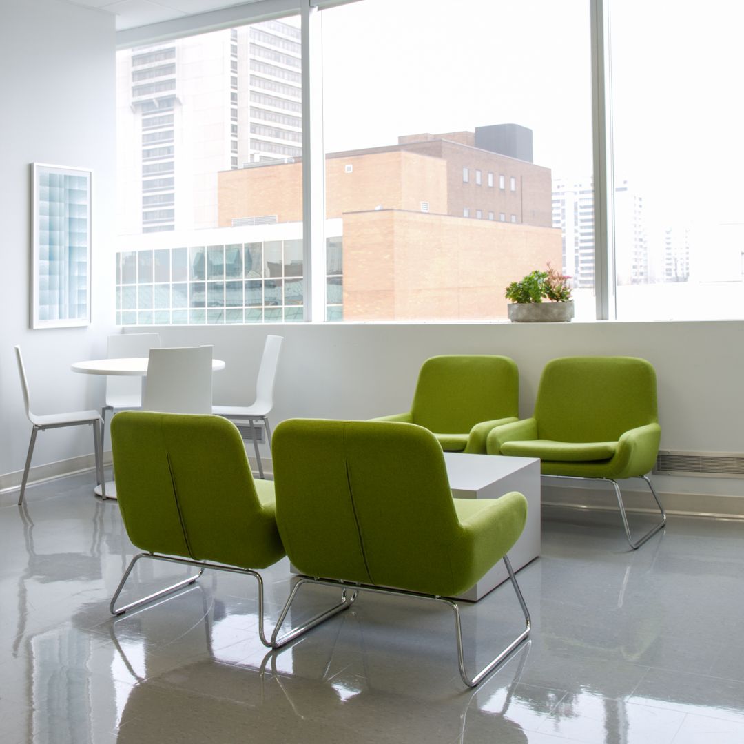 A waiting room with lime green armchairs, white table, and chairs near a large window overlooking a city.