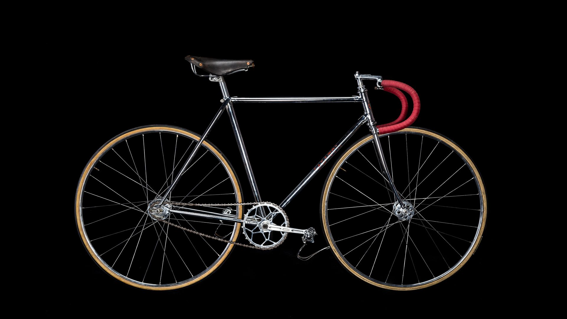 Silver fixed-gear bicycle with red handlebars and tan tires against a black background.