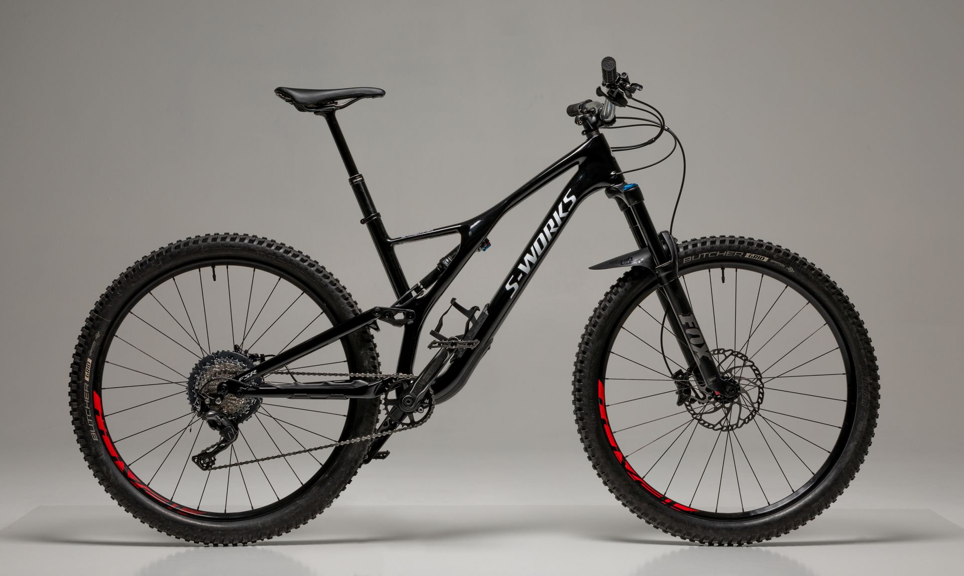 Black mountain bike with black tires and red rims against a gray backdrop.