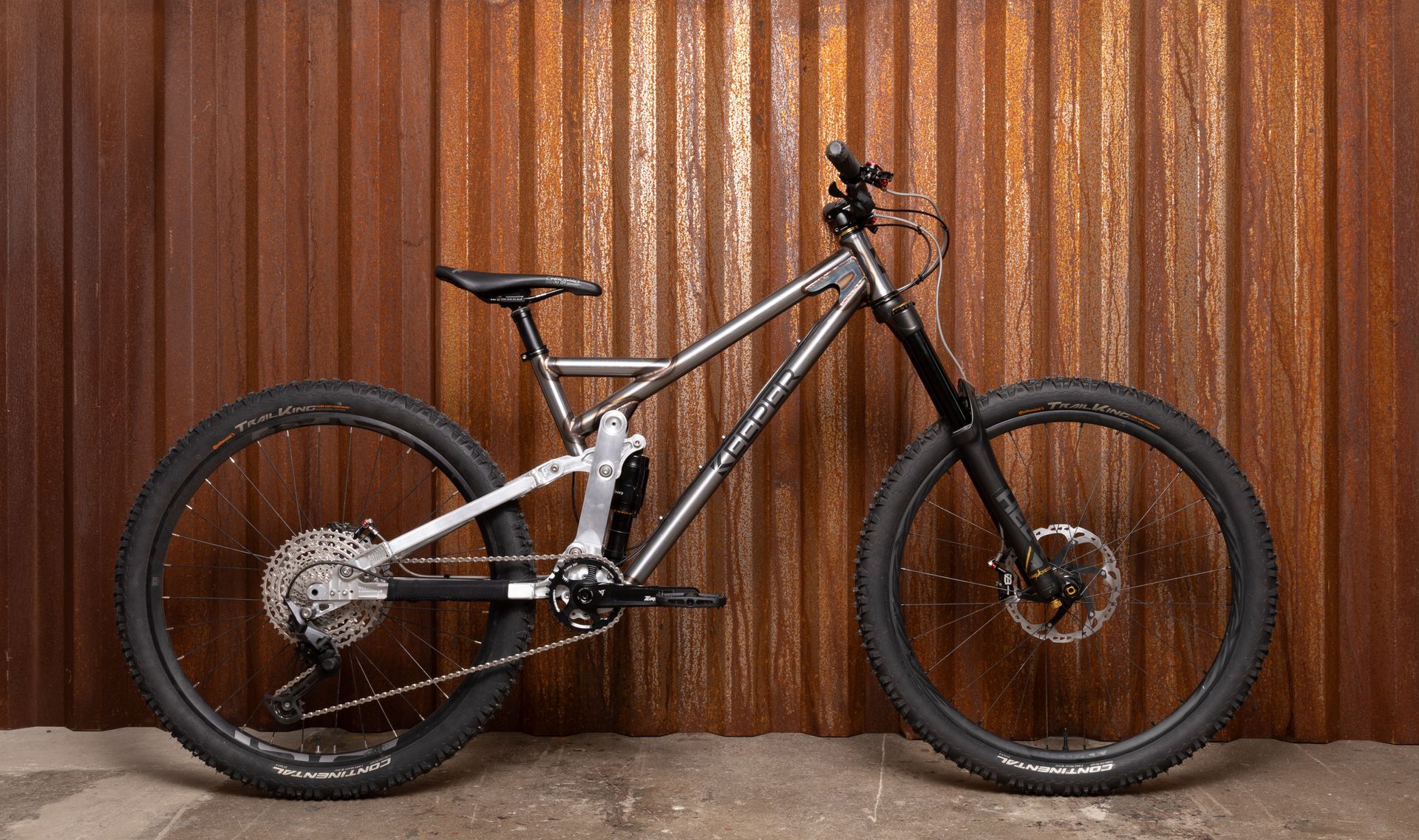 Silver mountain bike with black tires and components against a rusty metal wall.