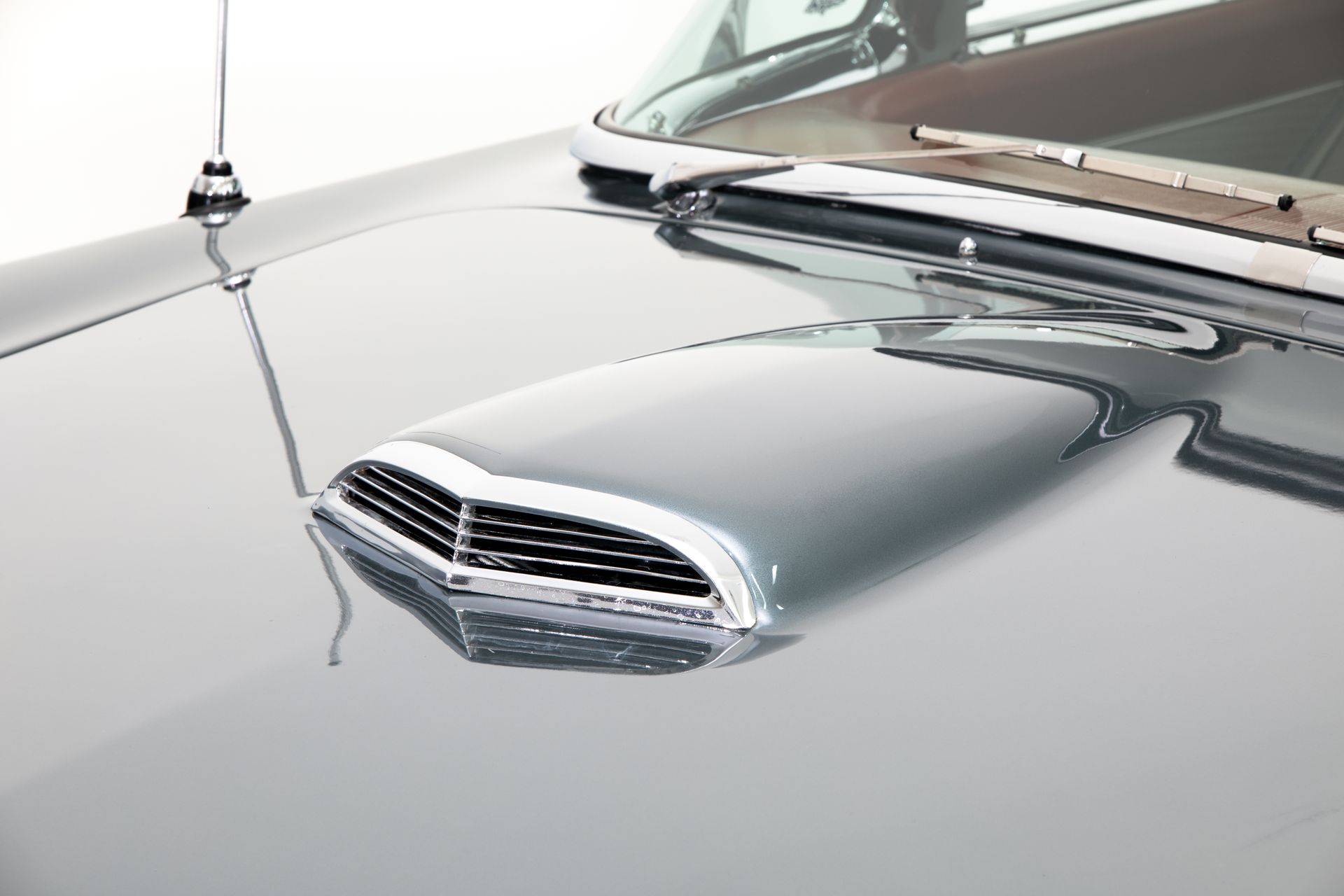 Gray car hood with a chrome-trimmed air scoop and antenna.