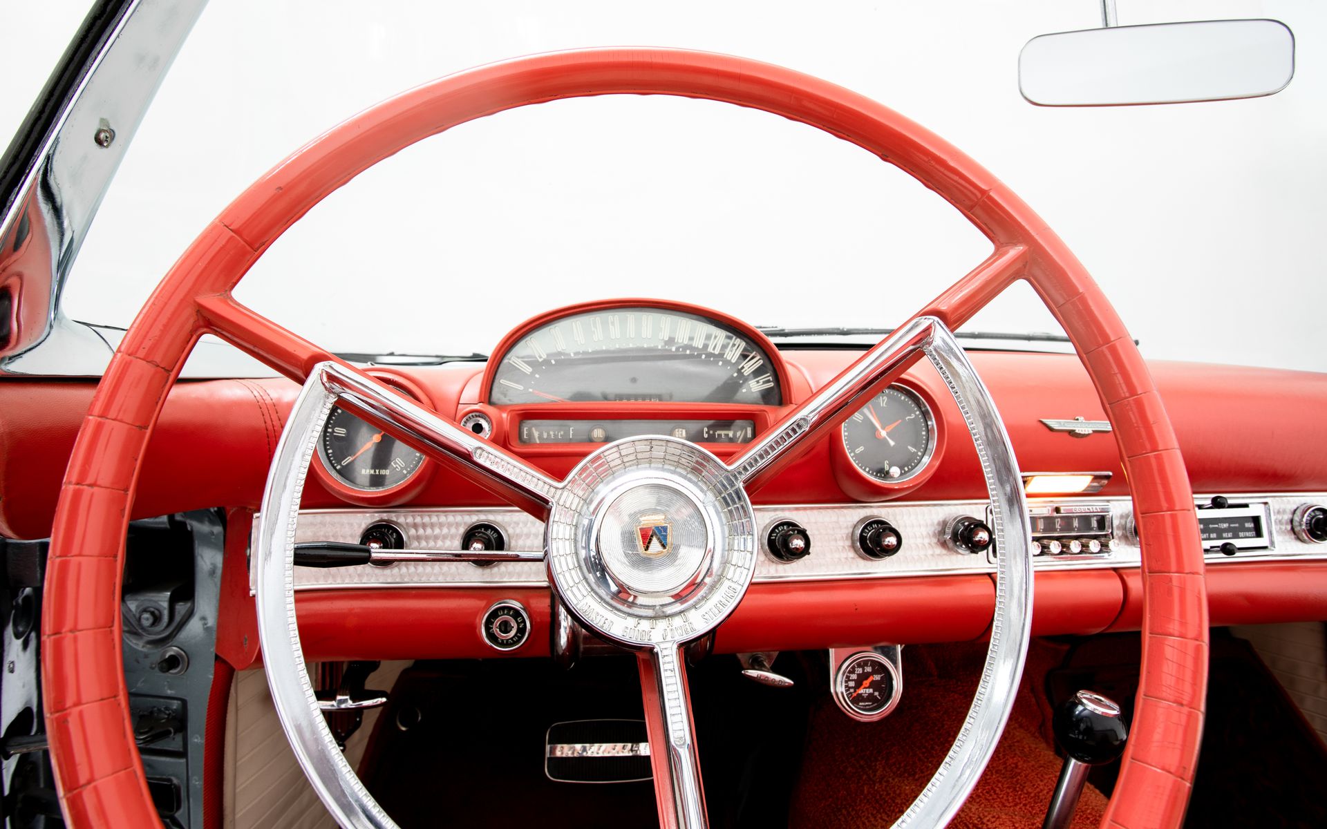 Red steering wheel and dashboard of a vintage car, with chrome accents and gauges.