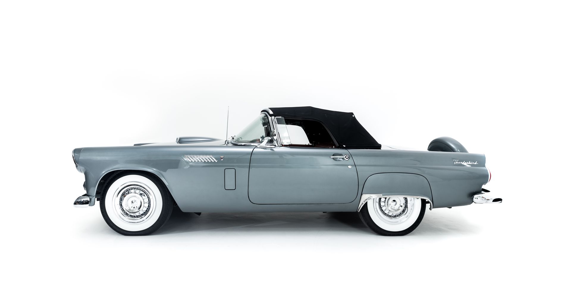 A gray convertible car with a black top on a white background.