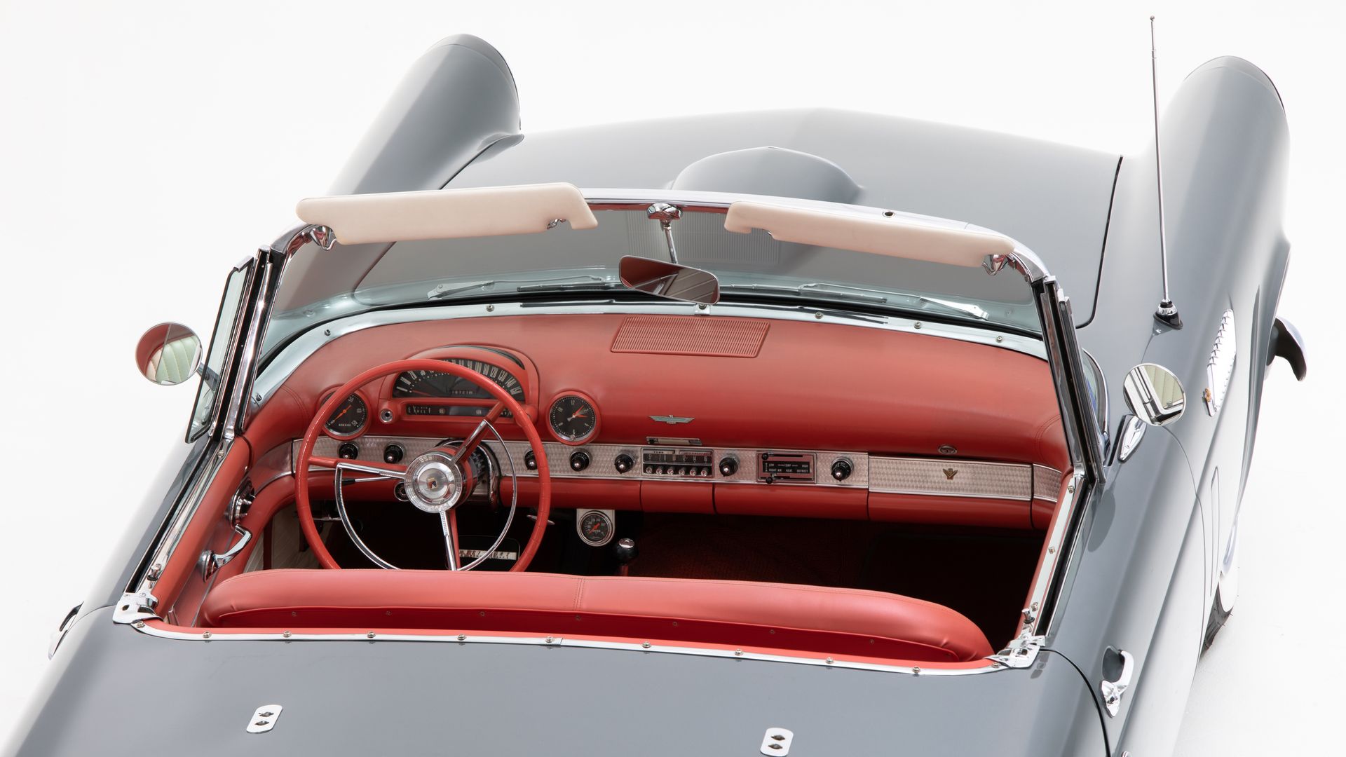 Gray classic convertible car interior with red dashboard and steering wheel.