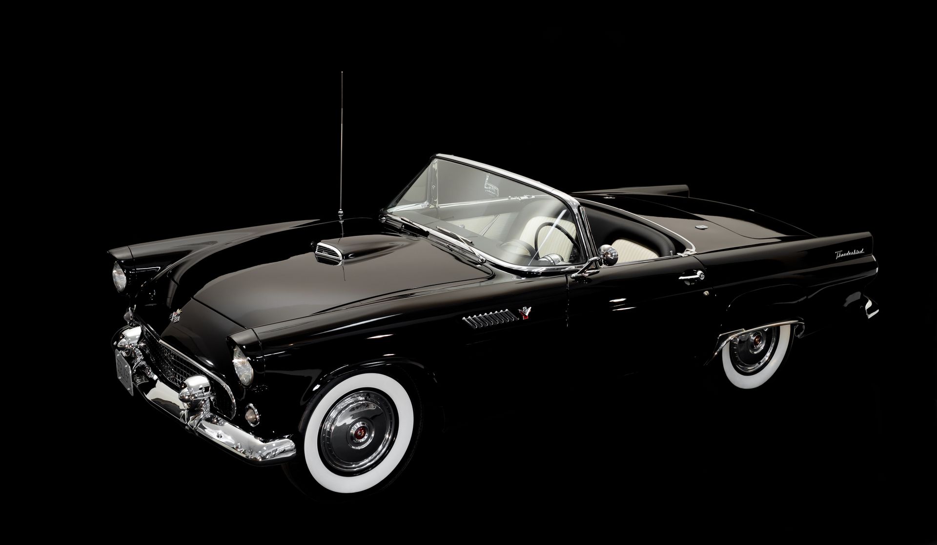 Black convertible car with white wall tires on black background.