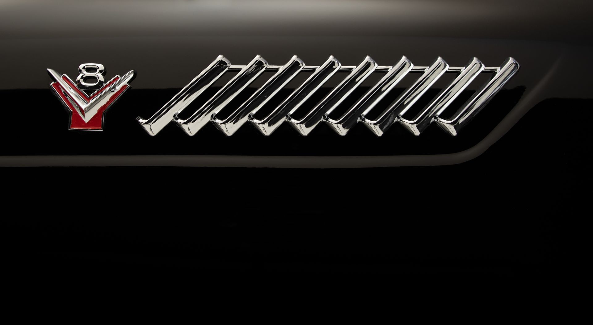 Chrome V8 emblem and angled chrome trim on black vehicle.
