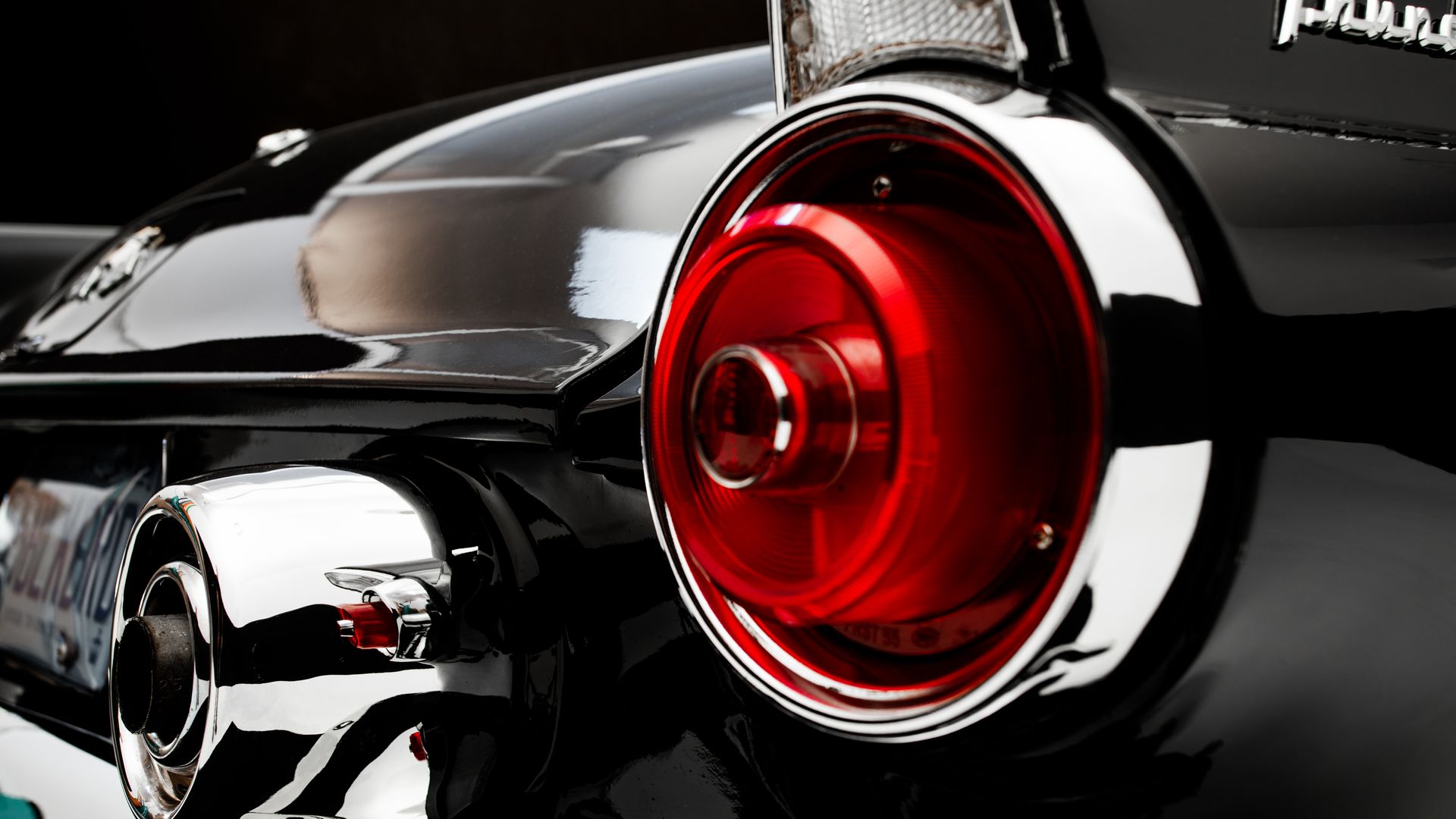 Close-up of a classic black car's red tail light with chrome accents.