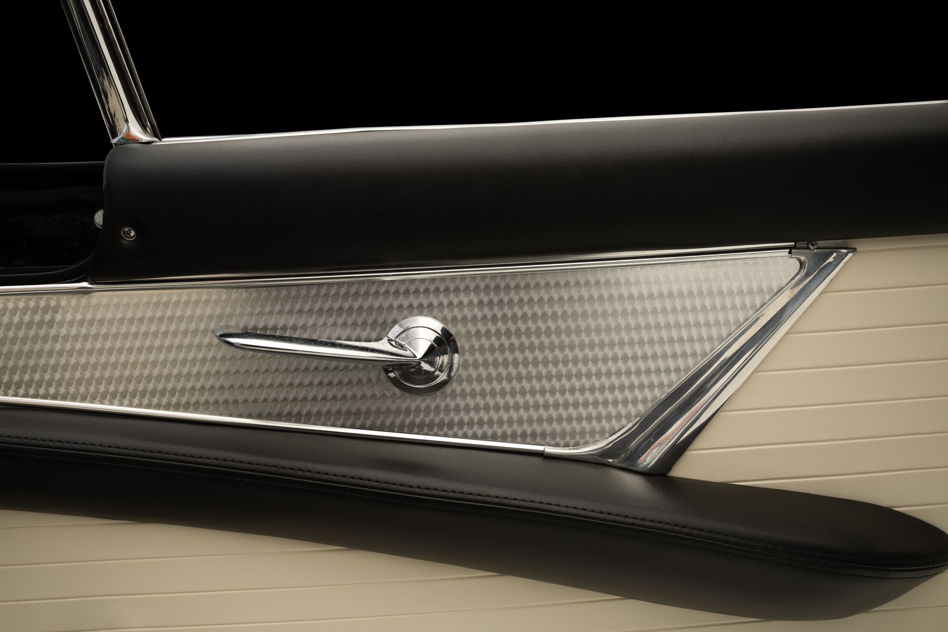 Close-up of a classic car door panel, with a chrome handle, textured silver and beige design.