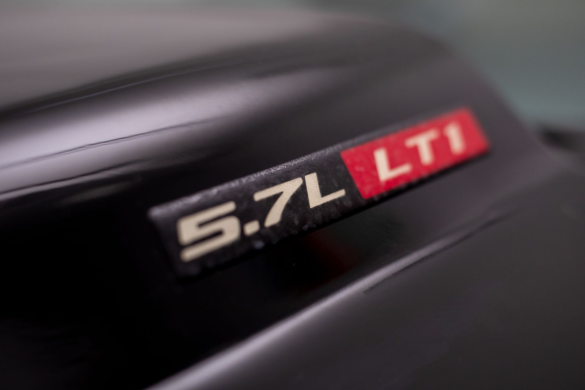 Close-up of a black car hood with a 5.7L LTI engine badge; white text on a red background.